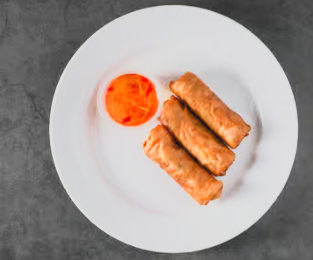 Three crisp lumpia rolls served on a white plate with dipping sauce